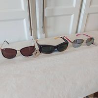 Three pairs of ladies style sunglasses displayed side by side on a light surface, showing various frame and lens styles and colors.