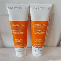 Two sealed tubes of Marcelle Vitamin C + PHA Brightening Cleanser standing upright, showing front labels with orange and white design.