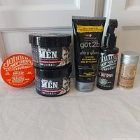 Photo showing all products arranged in a line: two Dippity-do Men pomade jars, Johnny's Chop Shop Wild Cat Clay tin, Schwarzkopf got2b Ultra Glued styling gel tube, Johnny's Chop Shop salt spray bottle, and Tigi Bed Head Hair Stick container.