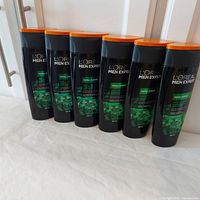 Six bottles of L'Oreal Men Expert Total Clean products displayed in a row on a flat surface, black bottles with orange caps.