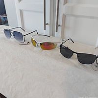 Photo showing all three men's sunglasses together on a white surface with tags visible.