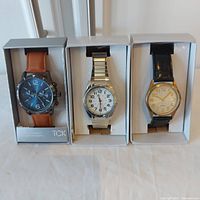 Three men's wristwatches in boxes: TCK quartz with brown strap and large blue dial, Precision quartz silver metal strap with white dial, Precision quartz black strap with white dial.