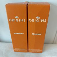 Lot of two Origins GinZing Glow-Boosting Serum boxes, bright orange packaging with Origins branding.