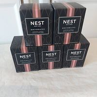 Five boxed Nest Rose Noir & Oud scented candles stacked in pyramid formation on plain surface