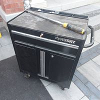 Front view of black Husky tool box, shows overall condition, locking drawer, chrome handles, and caster wheels