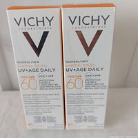 Photo of two boxed bottles of Vichy Capital Soleil UV+Age Daily SPF 60 anti-aging protective lotion, side by side showing front packaging with brand and product details.