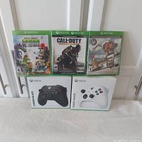 Two sealed Xbox wireless controllers in retail boxes (Carbon Black and Robot White), three sealed video game cases (Plants vs Zombies Garden Warfare, Call of Duty Advanced Warfare, Skate 3)