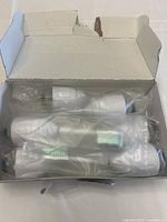 Photo of open white cardboard box containing six toothbrush replacement heads individually wrapped in clear plastic.