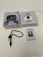 Photo showing M51 Bluetooth earbuds in white in molded plastic tray alongside product box, USB charging cable, and user manual.