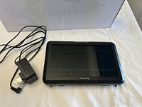 Front view of Dreamsky GPS navigation system with charger placed next to it on a white cloth surface.