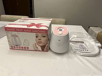 Photo showing the boxed smart fruit mask machine, unpacked device, mask tray, and instruction manual placed on a white table.