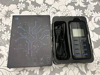 Top view of i8 USB charging station inside black packaging tray with power cord. Shows 8 blue USB ports and LCD screen.
