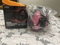 Photo of Józy brand noise protective ear muffs in pink and black still in plastic wrap with original packaging box beside it.