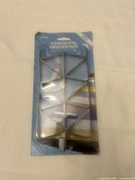 Front view of Pinnure branded stainless steel tablecloth clips in original packaging, showing 12 metal clips arranged in two vertical columns of six each on blue and white backing card.