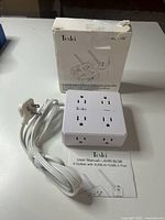 Front view of the Tcstei AHR-803B power strip with connected power cable, showing 8 outlets on top and sides, with box and user manual behind.