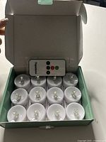 Open box showing twelve white LED tealights arranged neatly with a remote control inside.