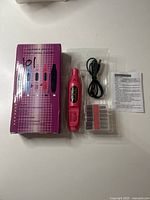 Photo showing pink rotary tool, its box, USB cable, bits set and instruction manual laid out on a white surface.