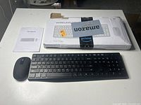 Wireless keyboard and mouse set laid out on white surface with user manual and damaged original box behind.