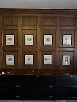 Eight framed prints displayed on wood-paneled wall