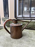 Overall view of copper watering can on stone ledge showing shape and patina