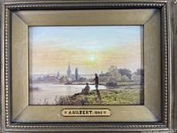 Close-up of framed painting depicting two men fishing at river with village in background, signed A. Gilbert 1885.