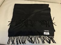 Full view of folded black scarf with fringed ends on light surface