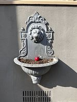 Full view of the wall mounted cast aluminum planter showing the lion motif and planter basin with some soil inside, along with light paint wear.