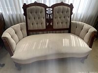 Front view of the antique settee showing the tufted backrest and seat with stains, carved wood frame, and cabriole legs.