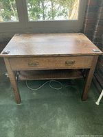 Full frontal shot of the oak desk showing drawer with brass handles, bottom shelf, and square wooden feet on desk corners.