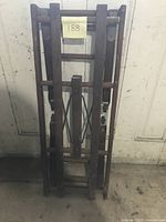 Folded vintage wooden wash tub stand leaning against a wall, showing the full stand folded slimly.