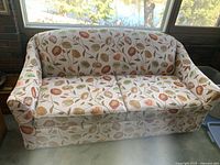 Front and side view of the beige floral patterned sofa bed with orange and green leaves design.