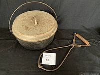 Solid cast iron Dutch oven with lid and vintage metal and wood tongs on a black background showing size and condition