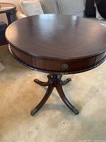 Front view of the circular wood parlour table showing round tabletop, carved pedestal, four legs with brass claw feet.