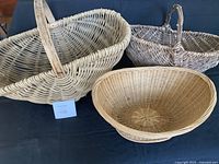 Three vintage wicker baskets displayed on dark surface, showing size differences and handle designs
