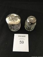 Two cut crystal vanity jars with silver embossed lids displayed on a black background with a MaxSold tag.