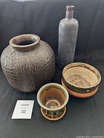 Four items: slate gray glass bottle vase, large brown crocodile skin textured vase, handmade ceramic bowl, and small artisan clay pot.