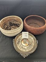 Three items: handmade ceramic pot with wear, red wood basket, silver-plated ornate serving tray with lid