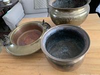Photo showing all three brass pots/planters on a wooden table, highlighting size variation and patina.