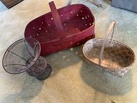 Three main items: red woven basket, smaller natural basket, and black wire vase on carpet.