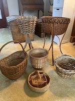 Wide view showing all seven baskets including two tall vintage plant stands and five other baskets on the carpet