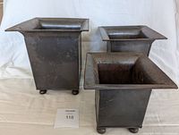 Three rustic metal square plant pots together showing their tapered square design and ball feet.