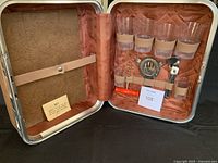 Open Samsonite picnic bar set case showing four plastic drinking glasses, two shot glasses, corkscrew, can opener, stirrer, strainer and key within quilted lining.