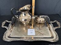 Entire laid out serving set on engraved tray with pitcher, butter dish, pickle fork, and small box visible. Background black fabric for contrast and ruler for scale.