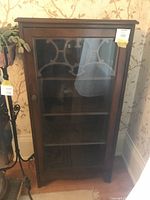 Full front view of the small wooden curio or china cabinet with glass door and decorative fretwork on the upper part of the glass panel.