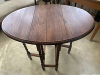 Oval solid wood drop leaf table with barley-twist legs, shown unfolded with gate legs deployed.