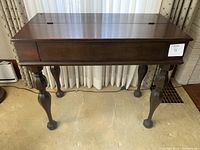 Front view of antique dark wood secretary desk with closed hinged top and ornate legs.