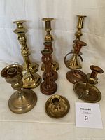 Six brass and two wooden candlesticks shown together on a light cloth background.