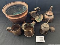 Wide view of vintage copper collection showing all six items including plant pot, coal shovel, two oil cans, fuel funnel, and stamped container.
