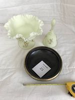 Three items on a white cloth: pale green ruffled custard bowl and dinner bell hand painted with white flowers, and a round ceramic candy dish with a metal rim and dark interior.