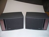 Front view of the pair of Bose 141 bookshelf speakers showing black mesh grille, gray housing, and side brown bass port accents.